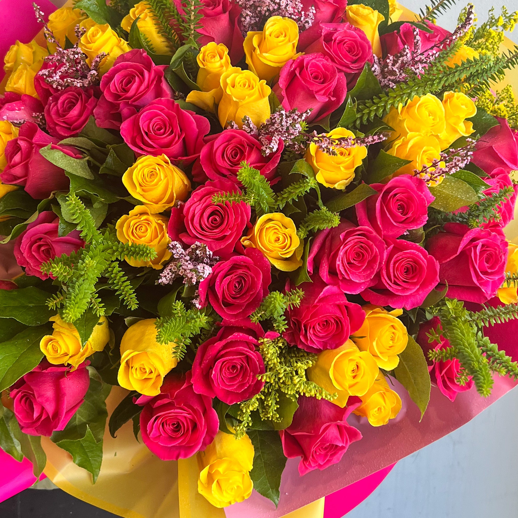 A vibrant bouquet of hot pink and yellow roses arranged in a matching pink and yellow vase, elegantly wrapped.