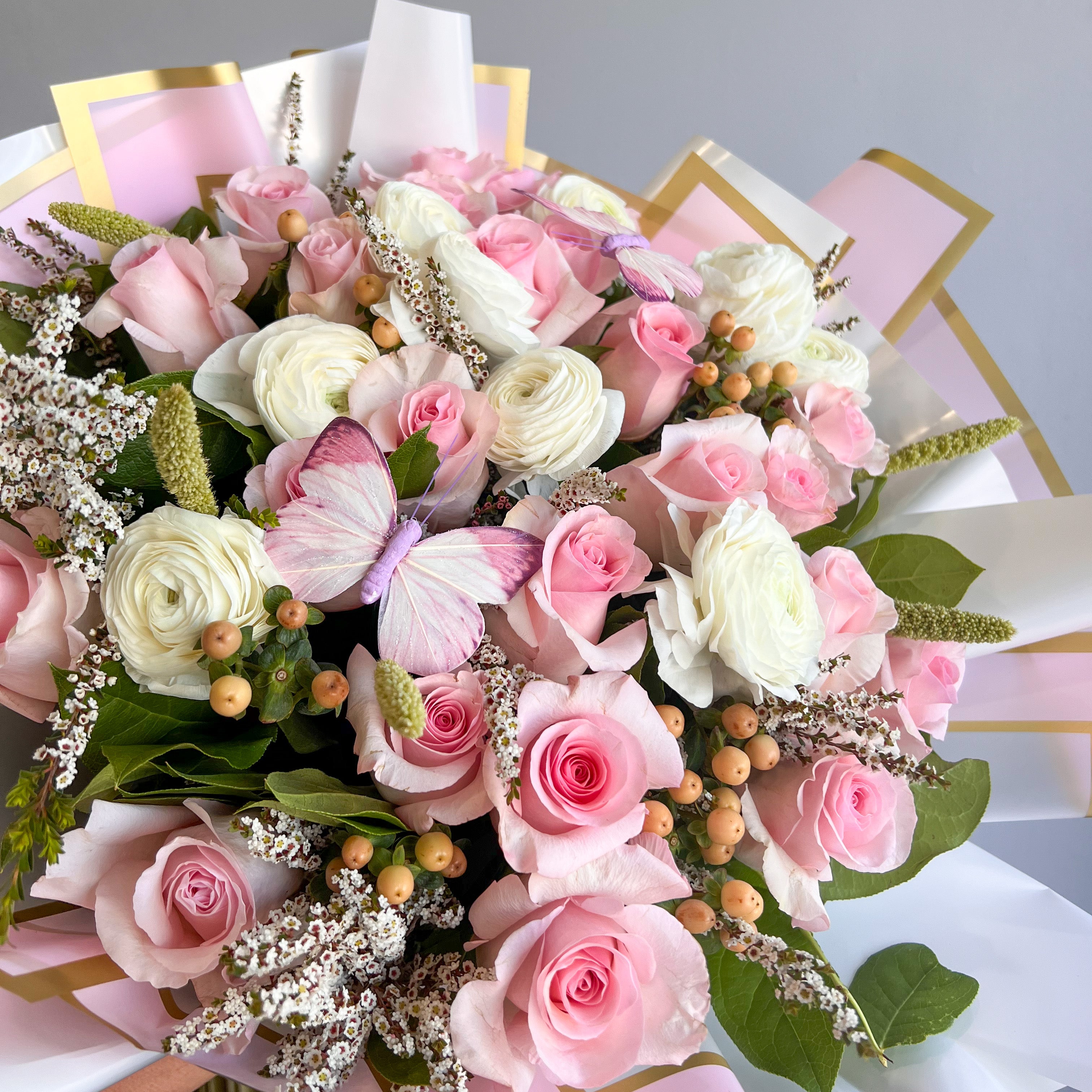 A beautiful bouquet of pink and white roses, along with ranunculus, elegantly wrapped for a stunning floral display