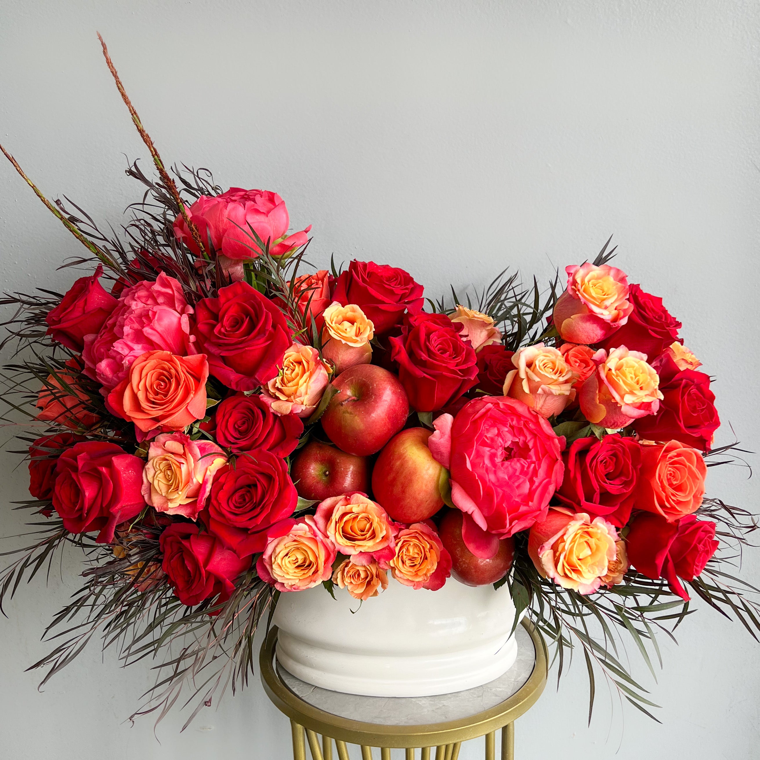 A white vase featuring lush red roses and bright apples, exemplifying a charming floral display