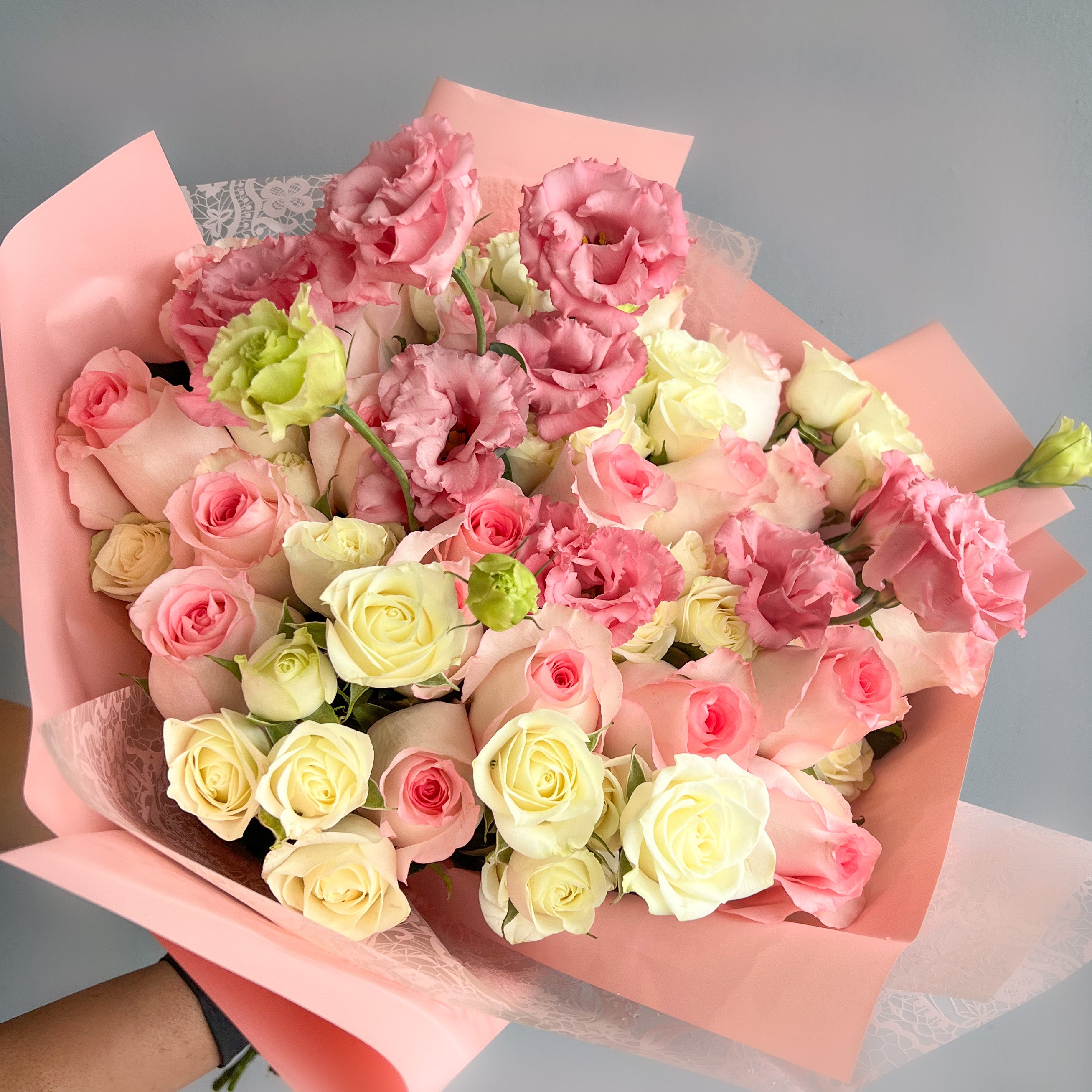 A hand holding Mariam's Signature Bouquet featuring pink and white roses elegantly wrapped together